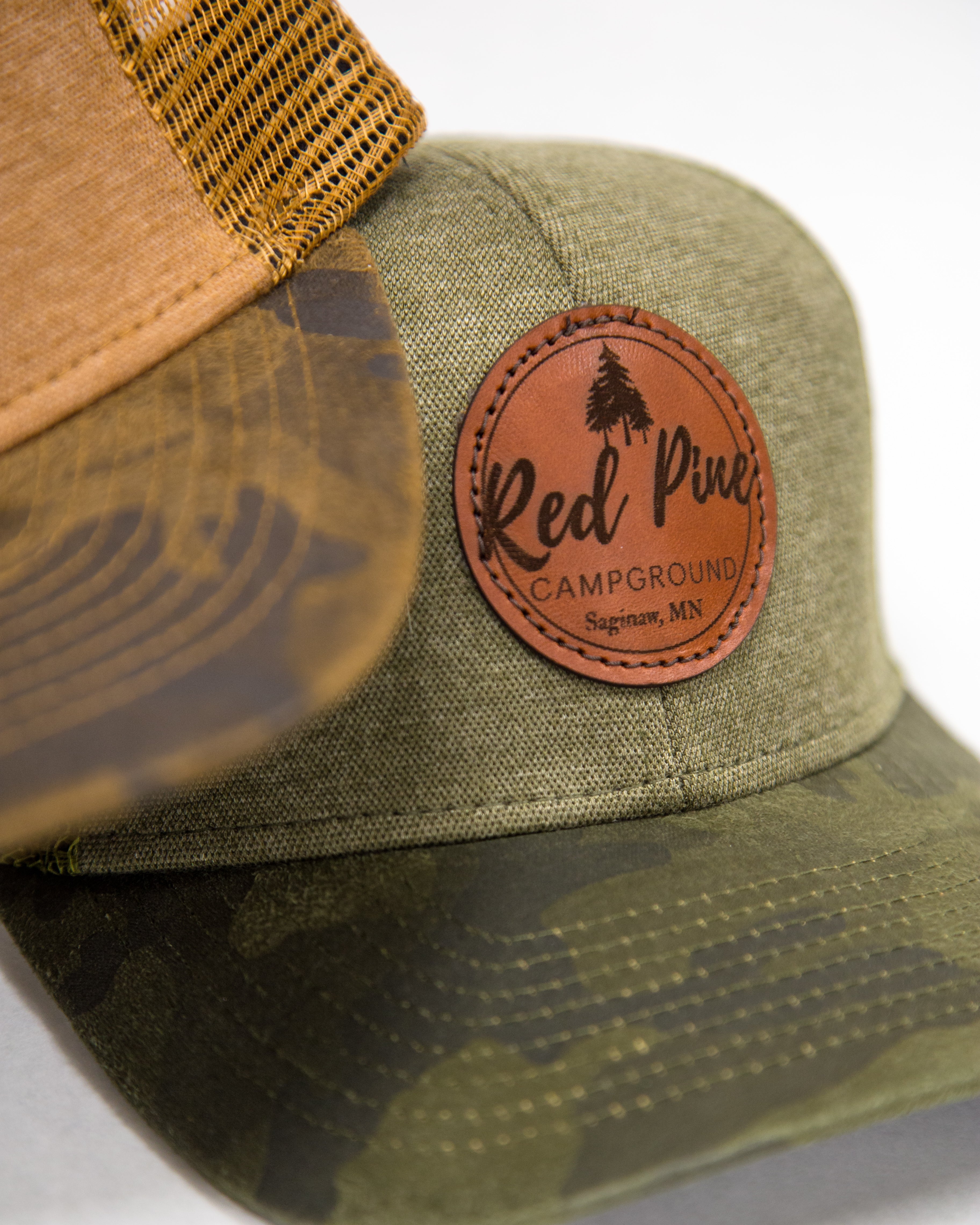 Two camo trucker hats with Red Pine Campground branded leather patches on the front.